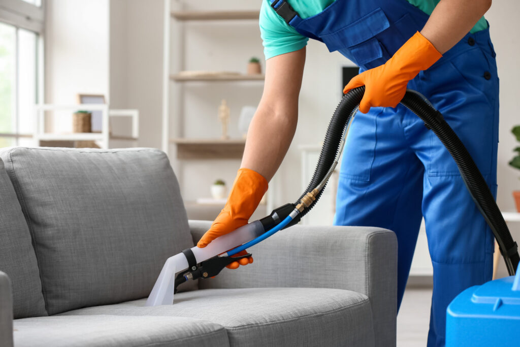 male worker removing dirty stain from grey sofa with vacuum clea